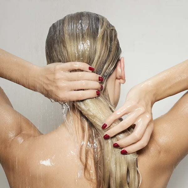 Blond woman washing her hair, showing freshly done red Dazzle Dry nails to highlight fast drying and durability.