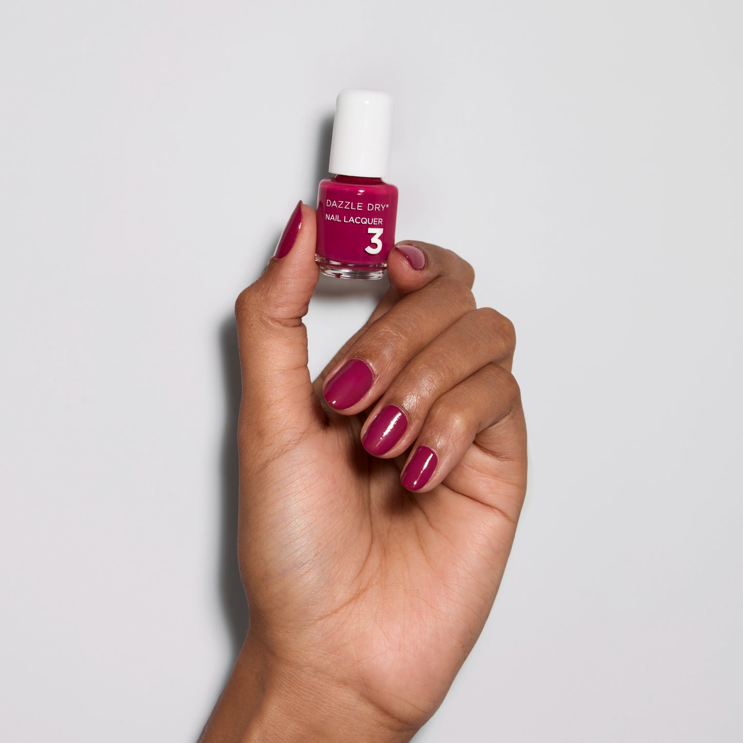 Hand with Raspberry Rush painted on nails holding mini nail lacquer bottle