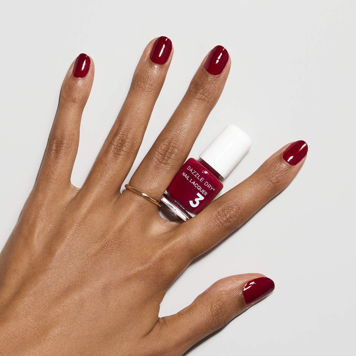 Hand with Fast Track Cherry painted on nails holding mini nail lacquer bottle