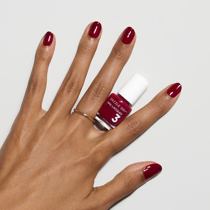 Hand with Fast Track Cherry painted on nails holding mini lacquer bottle