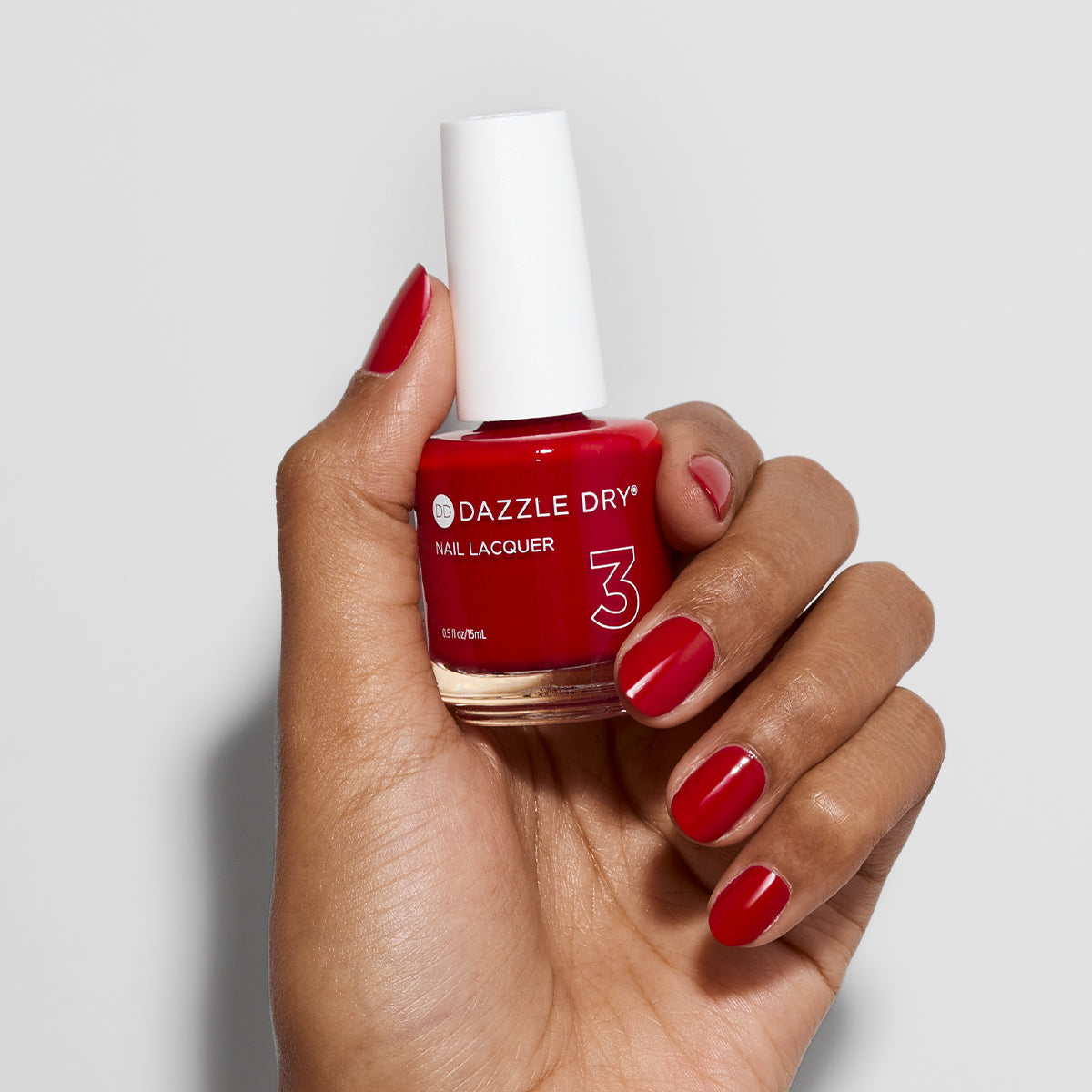 Hand with Rapid Red painted on nails holding lacquer bottle
