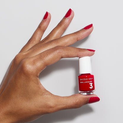 Hand with Rapid Red painted on nails holding mini lacquer bottle