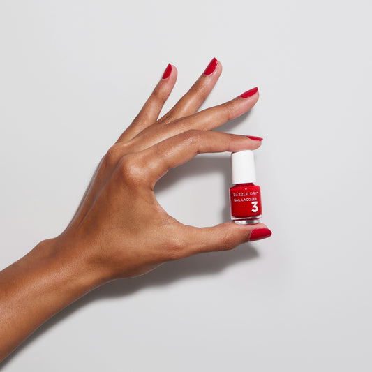Hand with Rapid Red painted on nails holding mini nail lacquer bottle