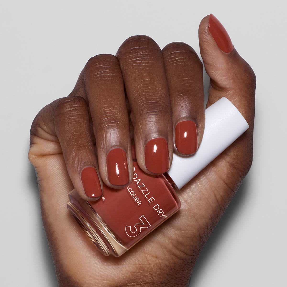Hand with Cinnamon Spice painted on nails holding nail lacquer bottle