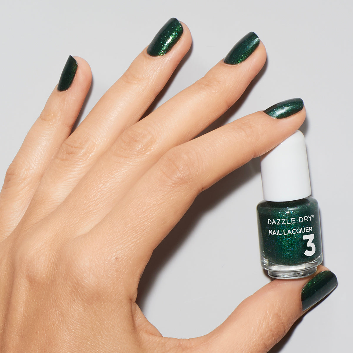 Hand with Evergreen painted on nails holding mini nail lacquer bottle