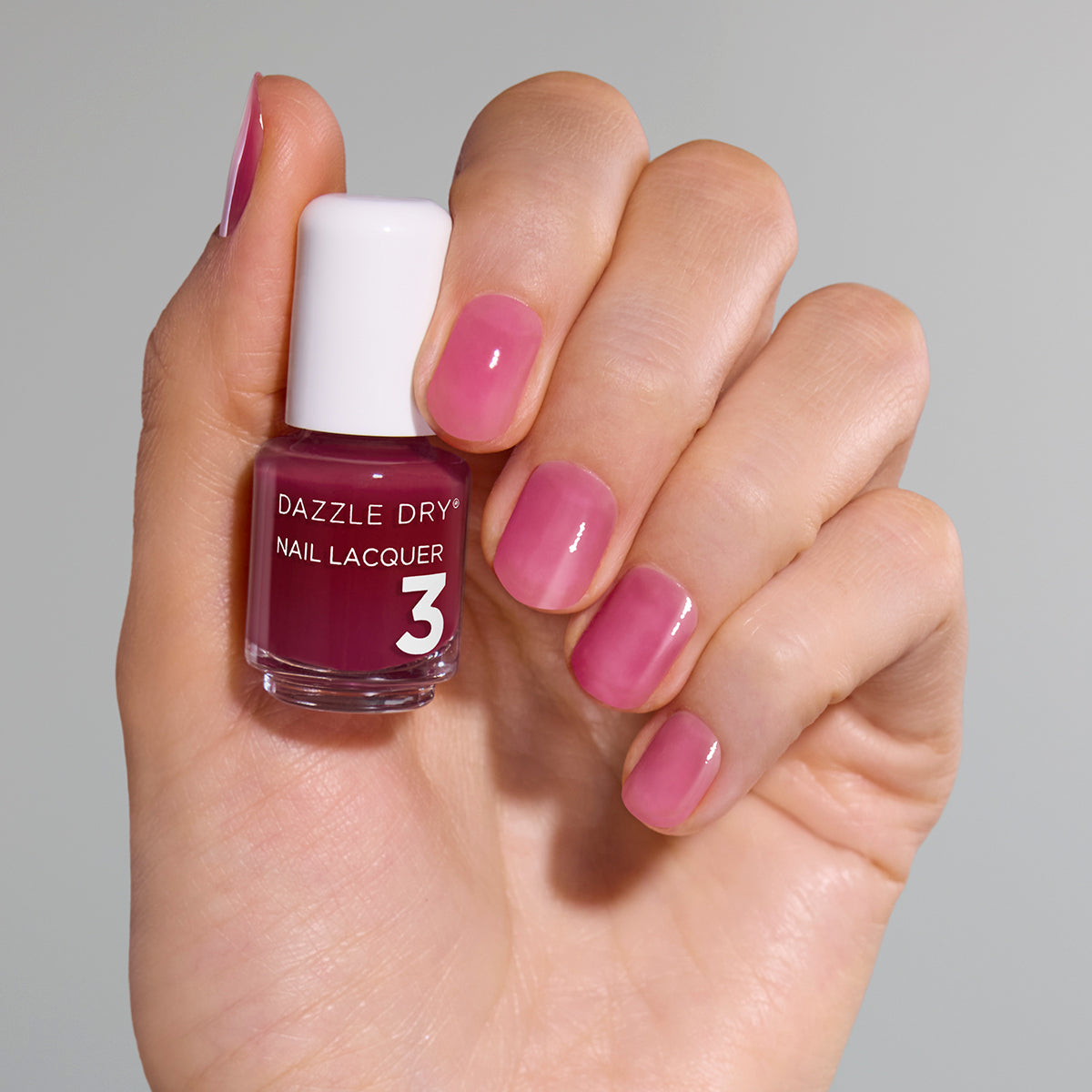 Hand with Ring Toss painted on nails holding mini nail lacquer bottle