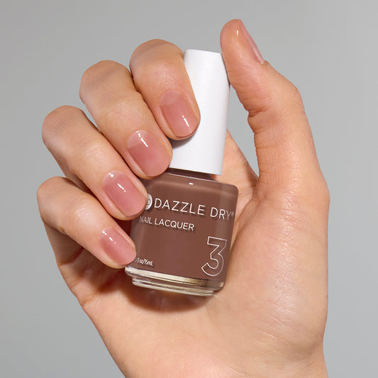 Hand with Toffee Crunch painted on nails holding full size lacquer bottle