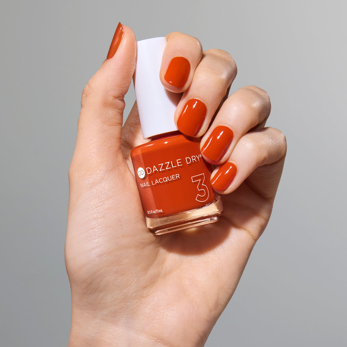 Hand with Orchard painted on nails holding full size lacquer bottle