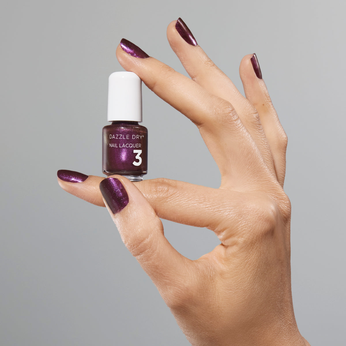 Hand with Spiced Plum painted on nails holding mini lacquer bottle