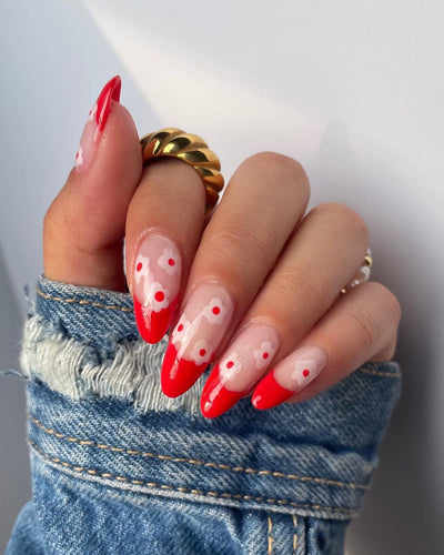 Hand with red painted nails on top and pink floral decoration with red.