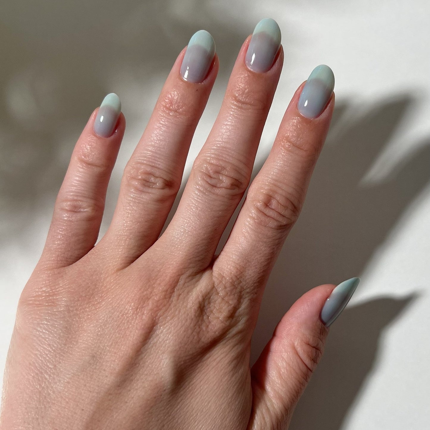 Hand with light gray nail polish on a neutral background
