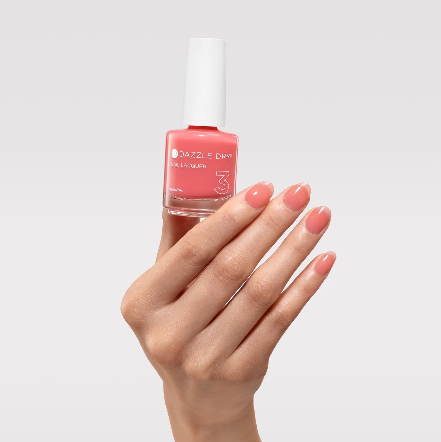Hand holding a bottle of Dazzle Dry nail polish with matching pink nails on a light gray background