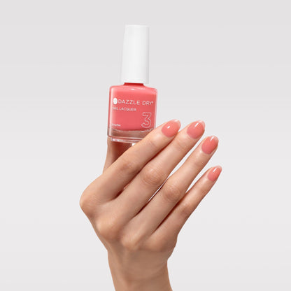 Hand holding a bottle of Dazzle Dry nail polish with matching pink nails on a light gray background
