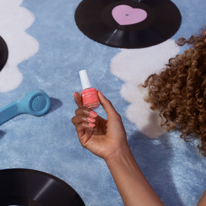 Hand holding a bottle of nail polish with vinyl records and a heart on a blue surface