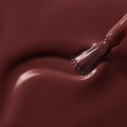 A close-up of glossy dark brown nail polish with a brush applying or smoothing the finish on a smooth surface.