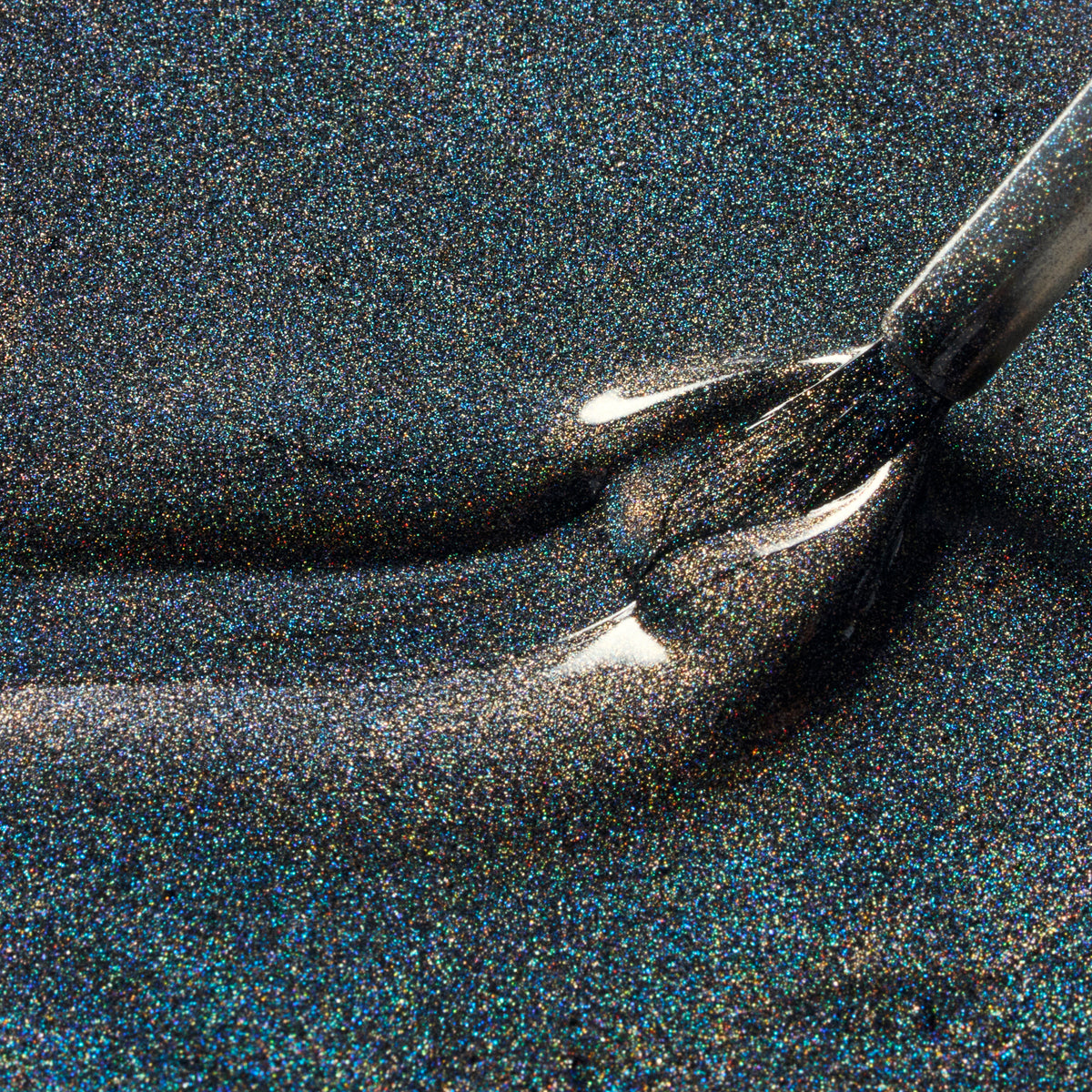 Close-up of a dark glitter nail polish brush applying shimmering black nail polish with fine iridescent flecks.