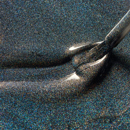 Close-up of a dark glitter nail polish brush applying shimmering black nail polish with fine iridescent flecks.