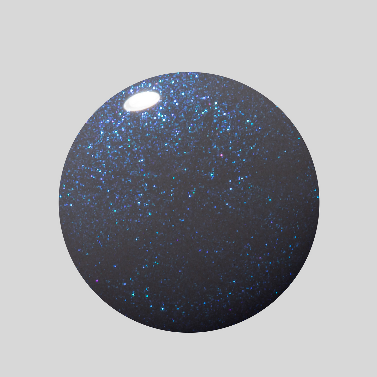 A circular swatch of dark navy glitter nail polish with shimmering blue and silver flecks, shown on a solid light gray background.