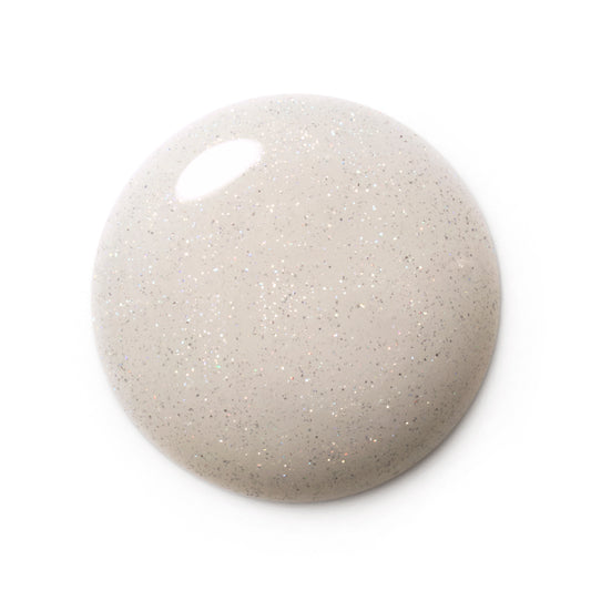 A glossy, rounded droplet of glittery nail polish in a light beige-gray shade with fine silver and gold flecks, shown on a solid white background.