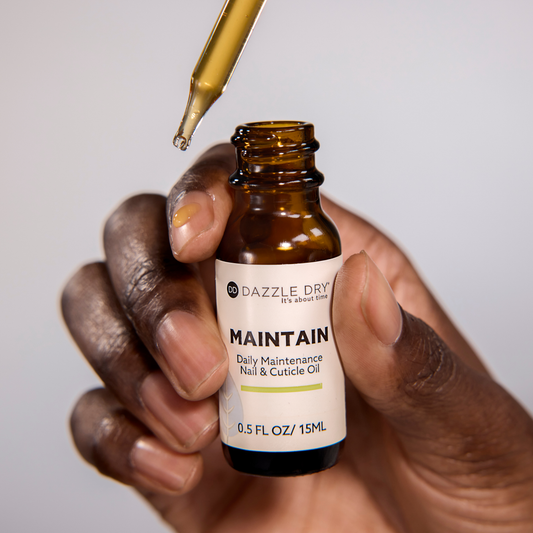 Hand holding a bottle of Dazzle Dry Maintain nail and cuticle oil with a dropper.