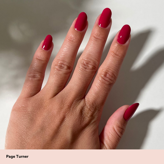 A close-up of a hand with glossy, almond-shaped nails painted in a deep berry red shade, labeled 'Page Turner' on a light beige banner at the bottom.