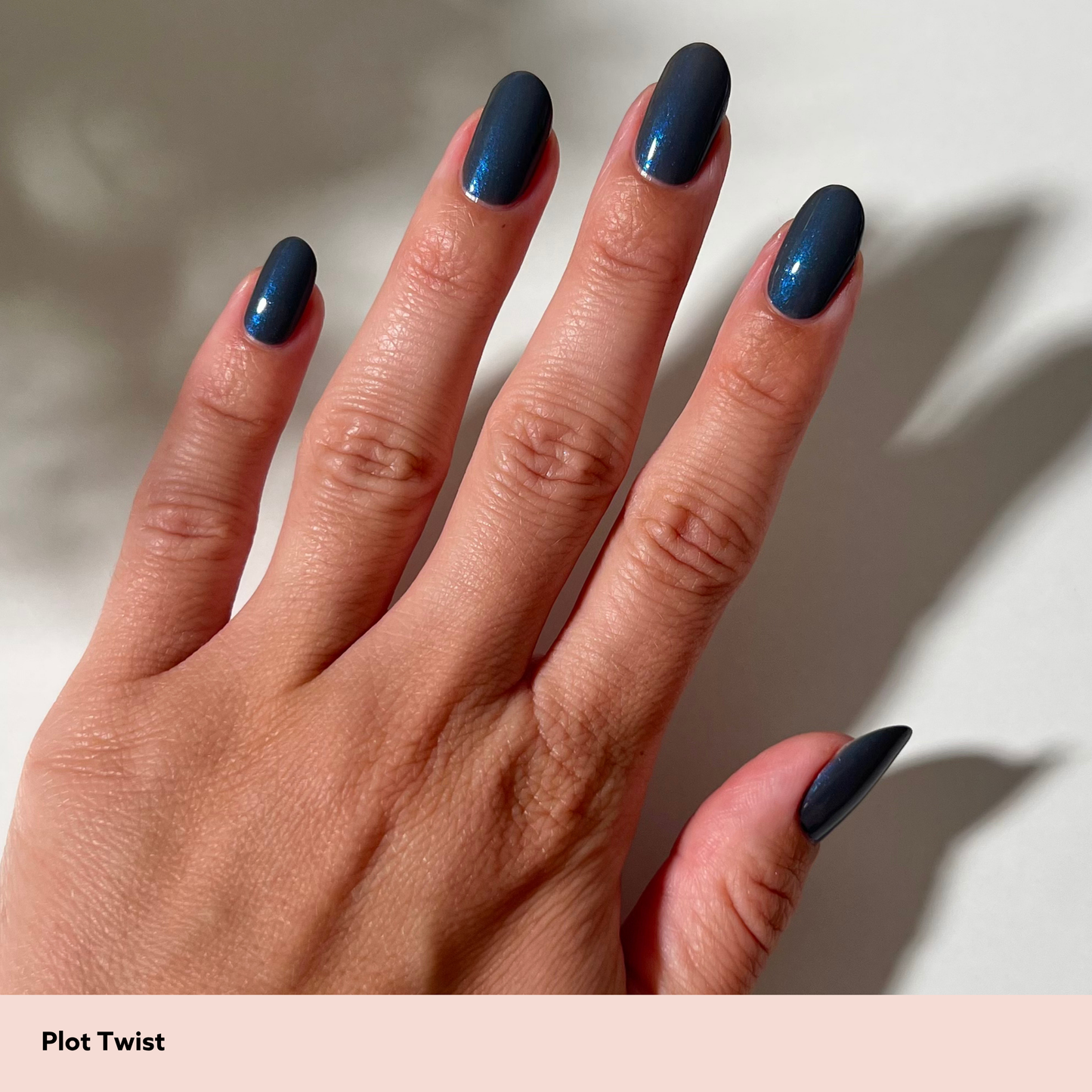 A close-up of a hand with long, almond-shaped nails painted in a deep metallic navy blue polish. The nails have a subtle shimmer and a soft gradient towards the tips.
