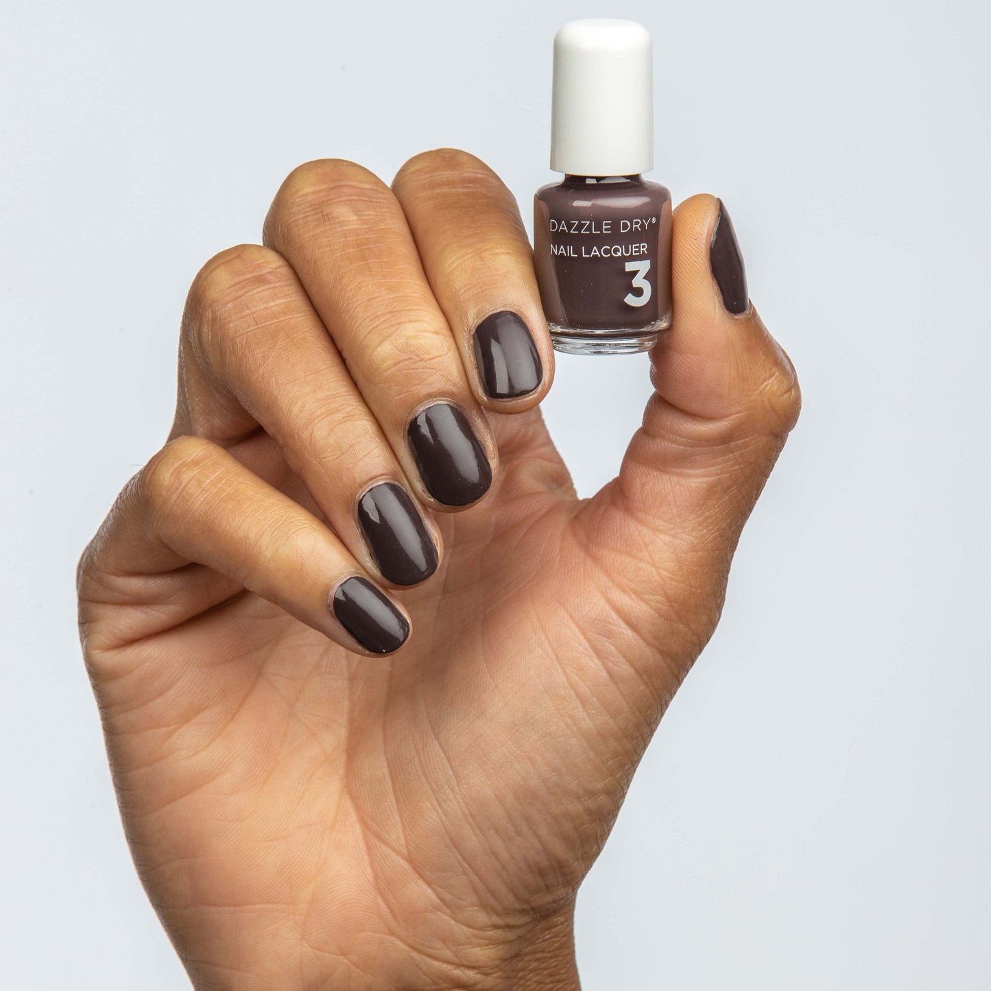 Hand with Rum Raisin painted on nails holding mini lacquer bottle