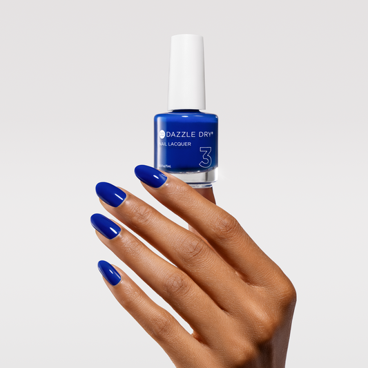 Blue nail polish bottle with a hand showcasing blue nails on a light gray background