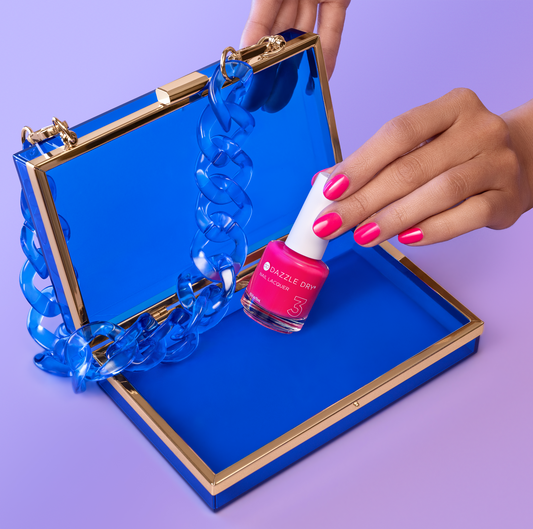 Hand with She's Electric painted on nails holding lacquer bottle inside blue purse.