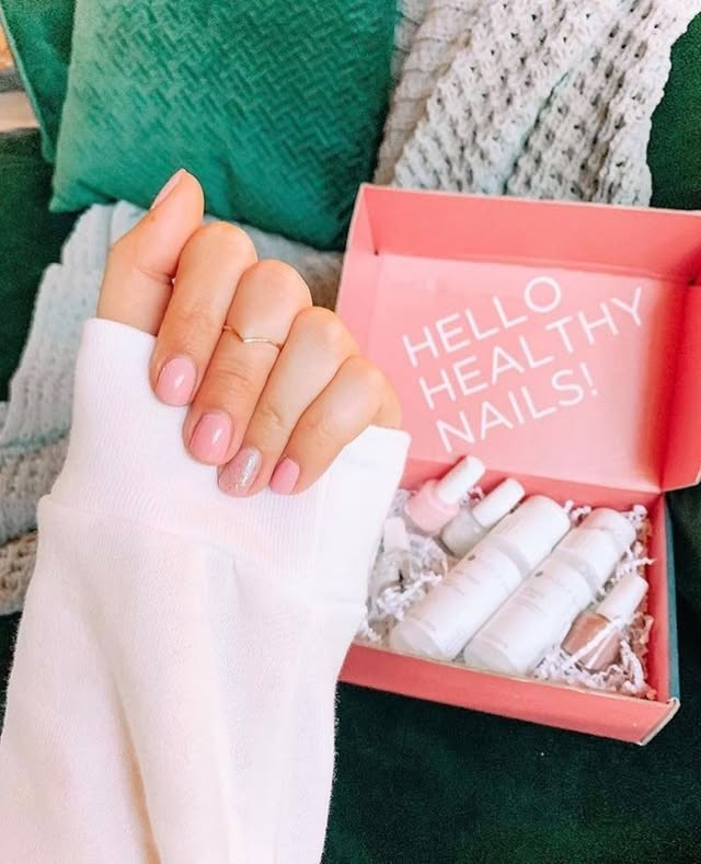 Close-up of hands with pink Dazzle Dry manicure unboxing an affiliate System box on a green couch