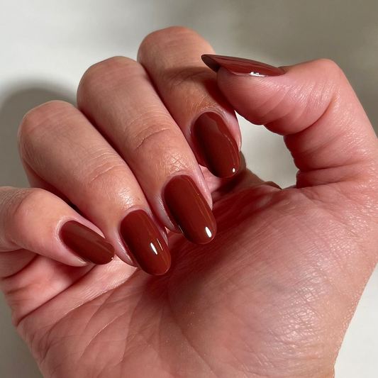 A close-up of a hand with glossy, almond-shaped nails painted in a warm, deep reddish-brown shade.