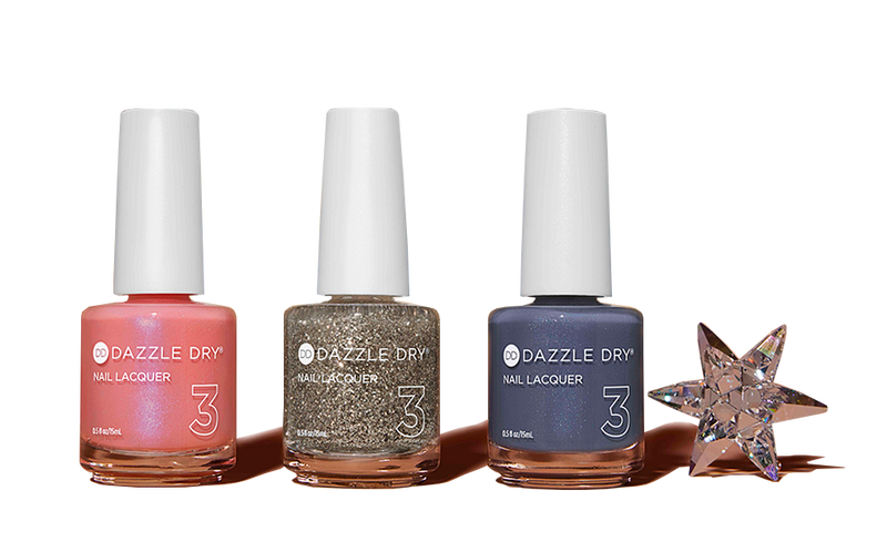 Three bottles of nail lacquer, one bright pink, one gold with glittery sparkles, and one deep blue, with a small shiny glass-like star next to them.