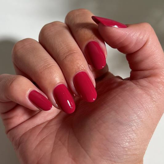 A close-up of a hand with long, almond-shaped nails painted in a glossy, deep berry pink nail polish.