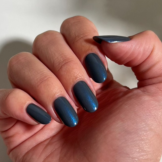 A close-up of a hand with manicured nails painted in a dark metallic blue-gray color with a subtle shimmer.