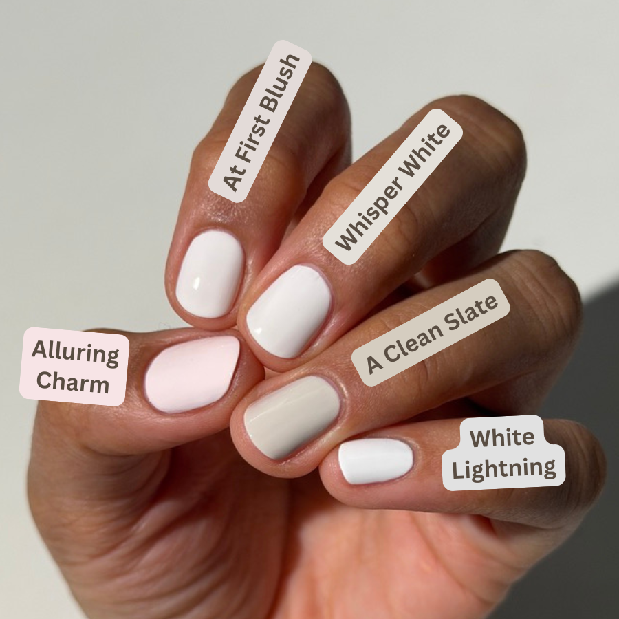 A close-up of a hand displaying five different nail polish shades with handwritten labels: 'Alluring Charm', 'At First Blush', 'Whisper White', 'A Clean Slate', and 'White Lightning'.
