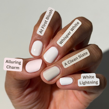 A close-up of a hand displaying five different nail polish shades with handwritten labels: 'Alluring Charm', 'At First Blush', 'Whisper White', 'A Clean Slate', and 'White Lightning'.