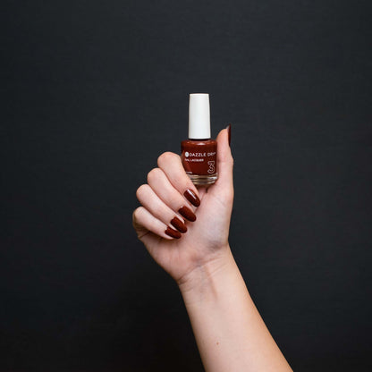 Hand with Siena painted on nails holding lacquer bottle